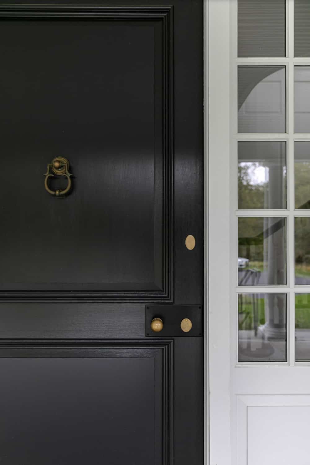 Close-up of black front door with brass ring knocker and knob beside a paneled sidelight window