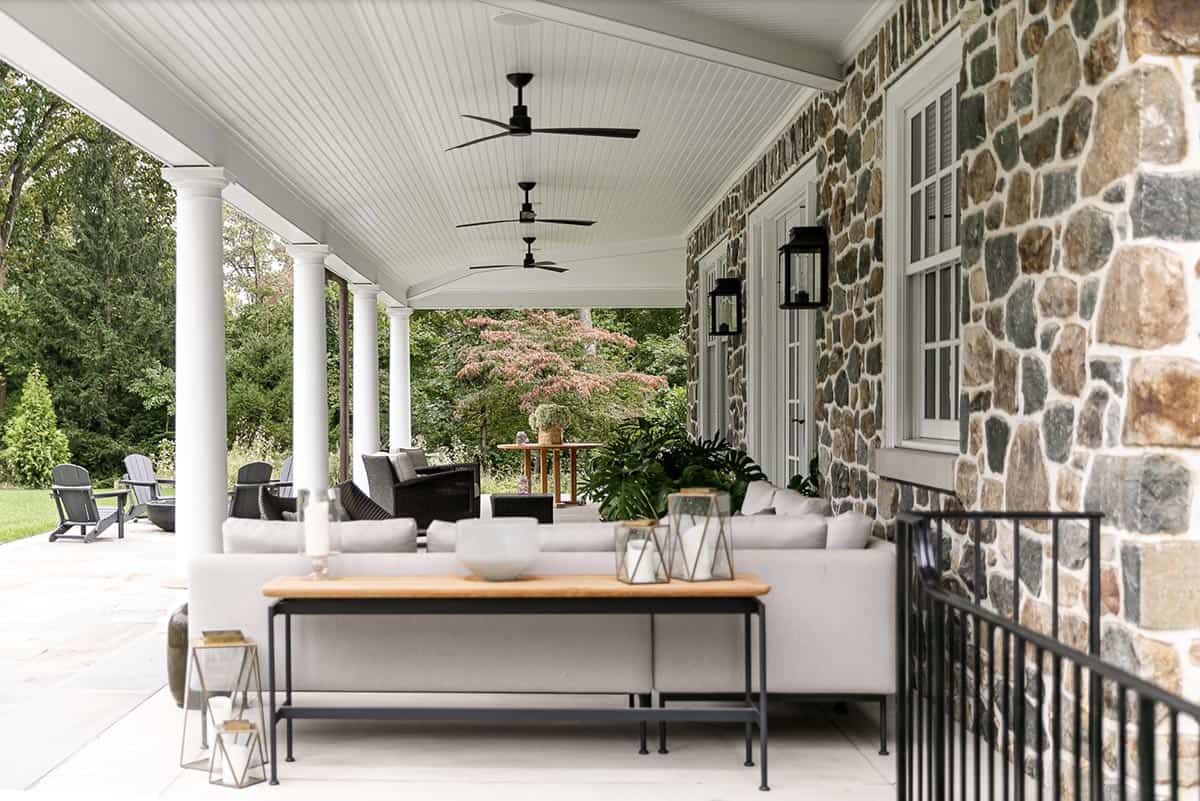 Covered stone porch with ceiling fans, lantern sconces, and a gray outdoor sectional