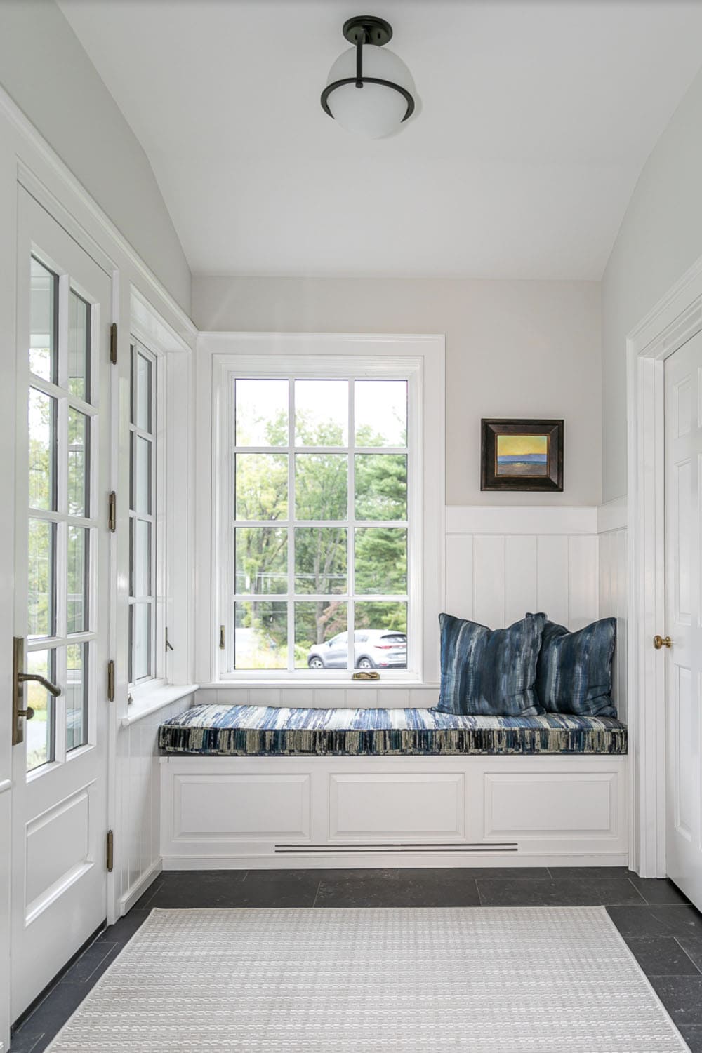 Mudroom nook with built-in window seat, striped blue cushions, and slate floor tile