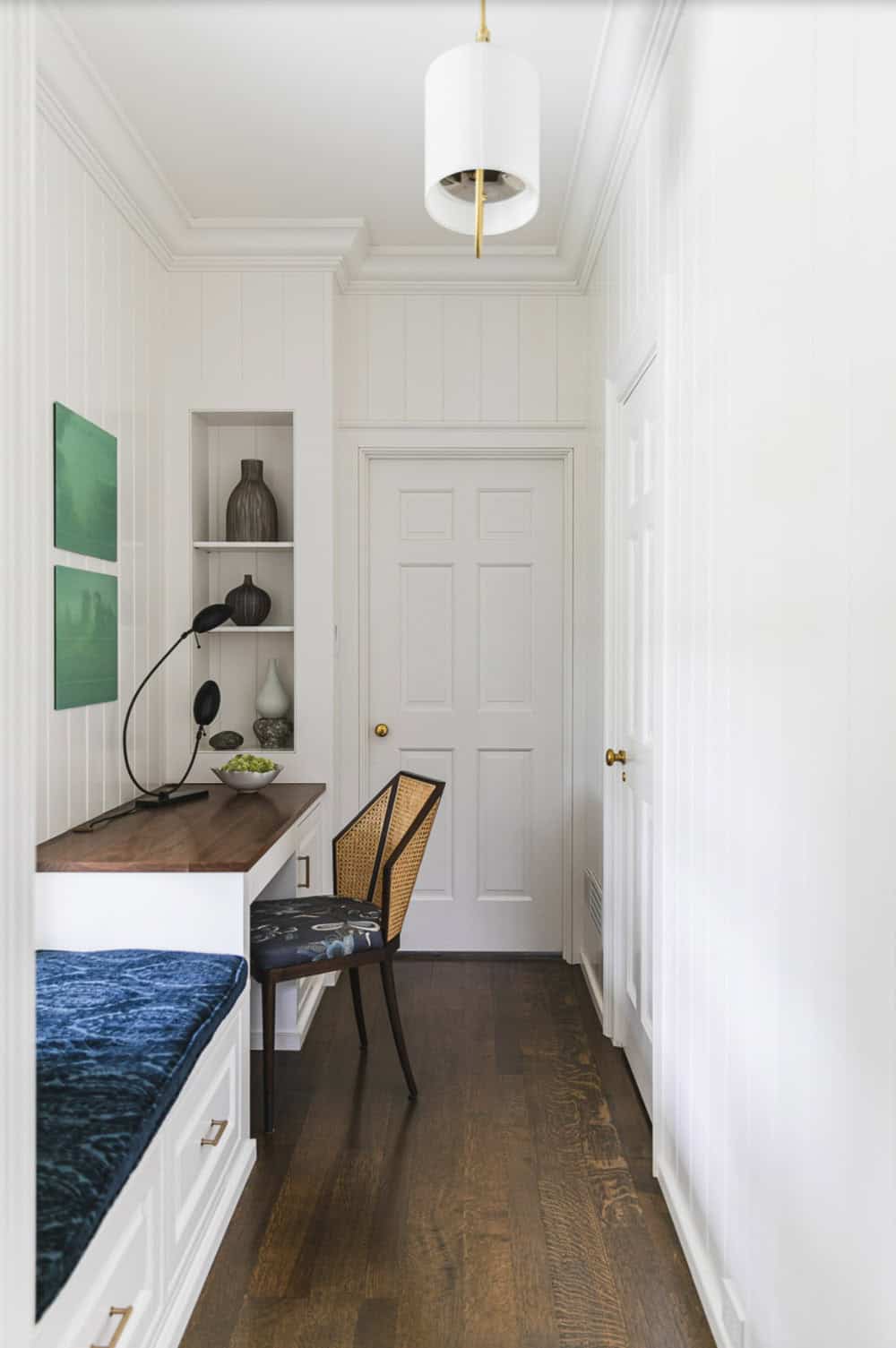 Narrow built-in desk nook with cane-back chair, walnut countertop, and pendant light