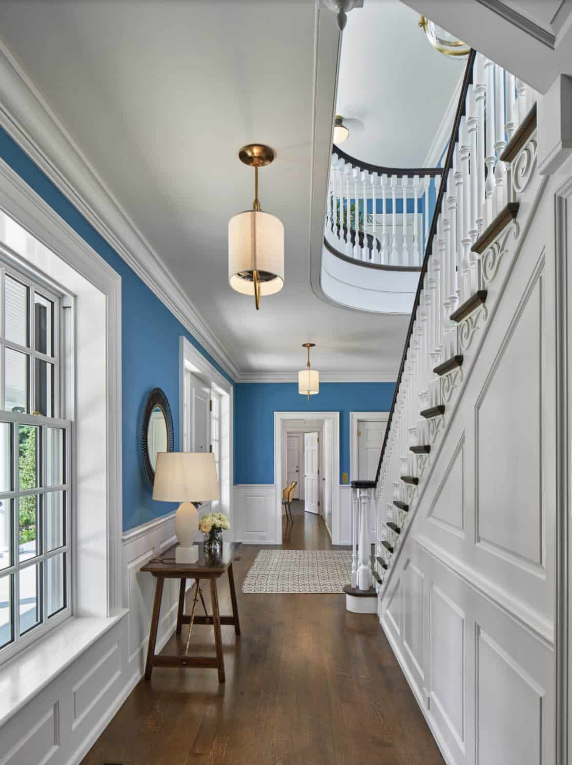 Upstairs hallway with blue walls, curved staircase railing, and brass pendant lights