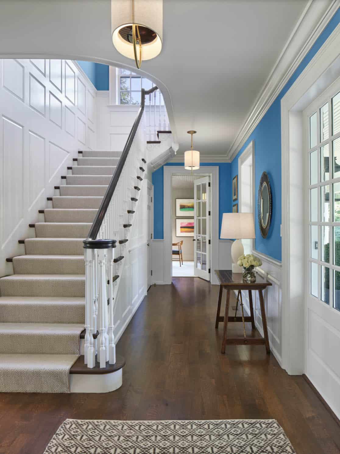 Staircase and hallway view showing blue walls, wood floors, and console table with lamp