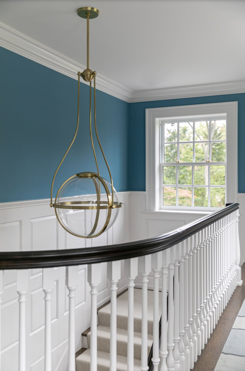 Curved stair landing with brass globe pendant light and blue wainscoted walls