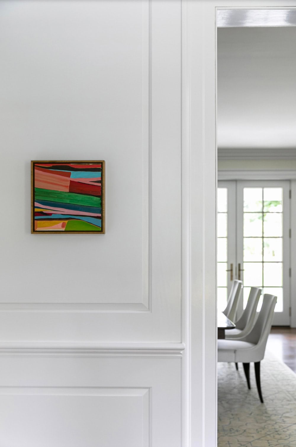Colorful abstract landscape painting on paneled wall beside doorway to dining room