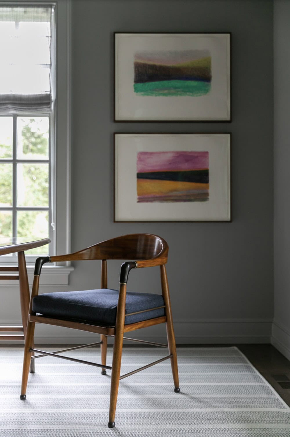 Mid-century armchair beneath two framed abstract landscape artworks on a gray wall