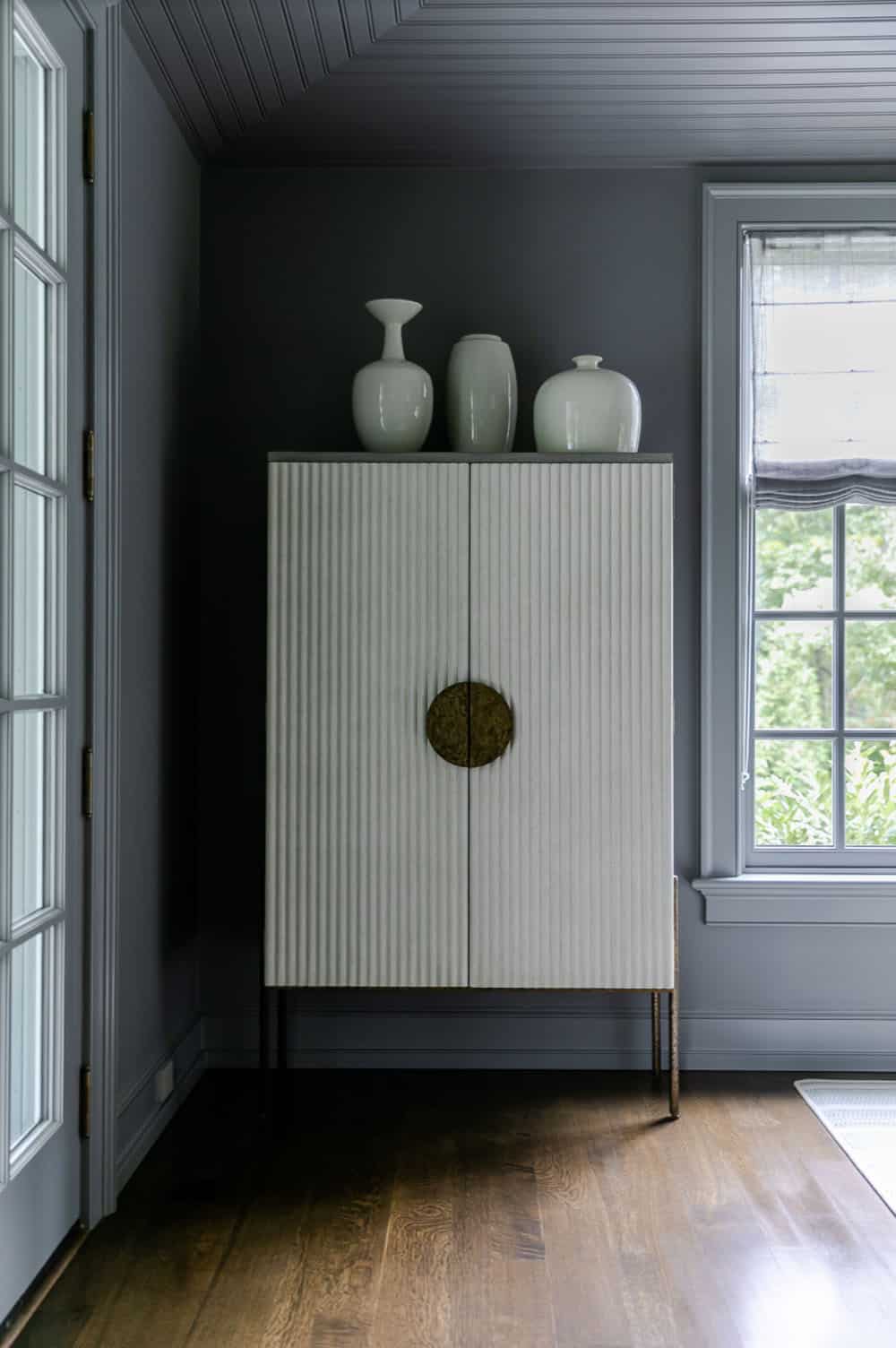 Dark charcoal room with fluted cabinet, ceramic vases, and window with woven roman shade
