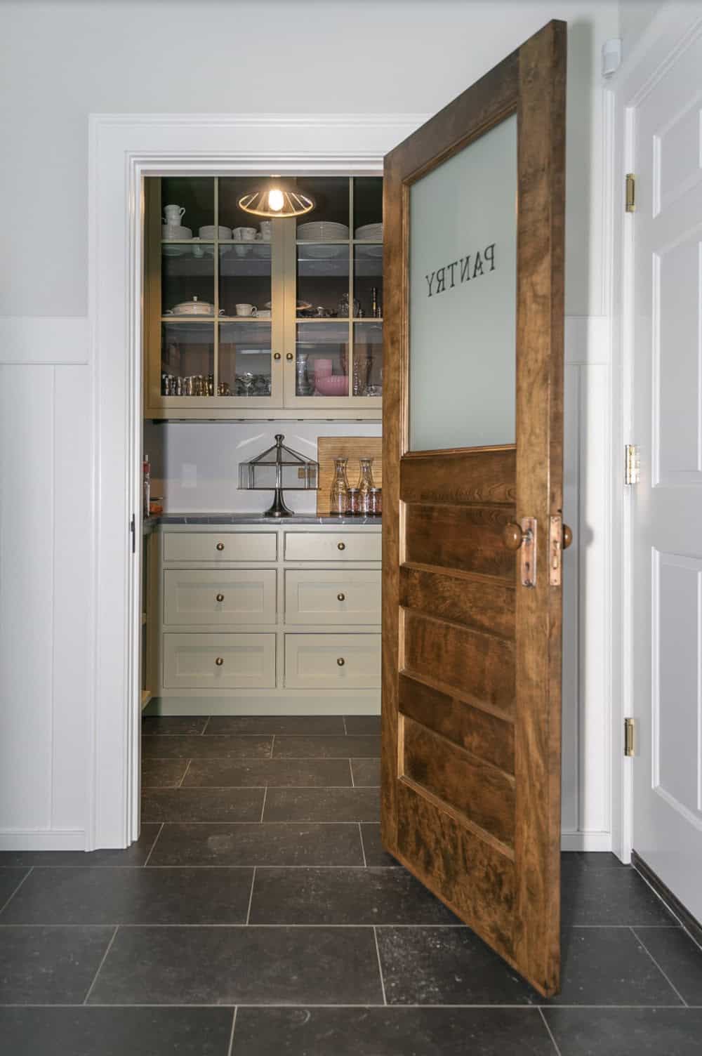 Open wood pantry door reading "Pantry" leading to butler's pantry with glass-front cabinets