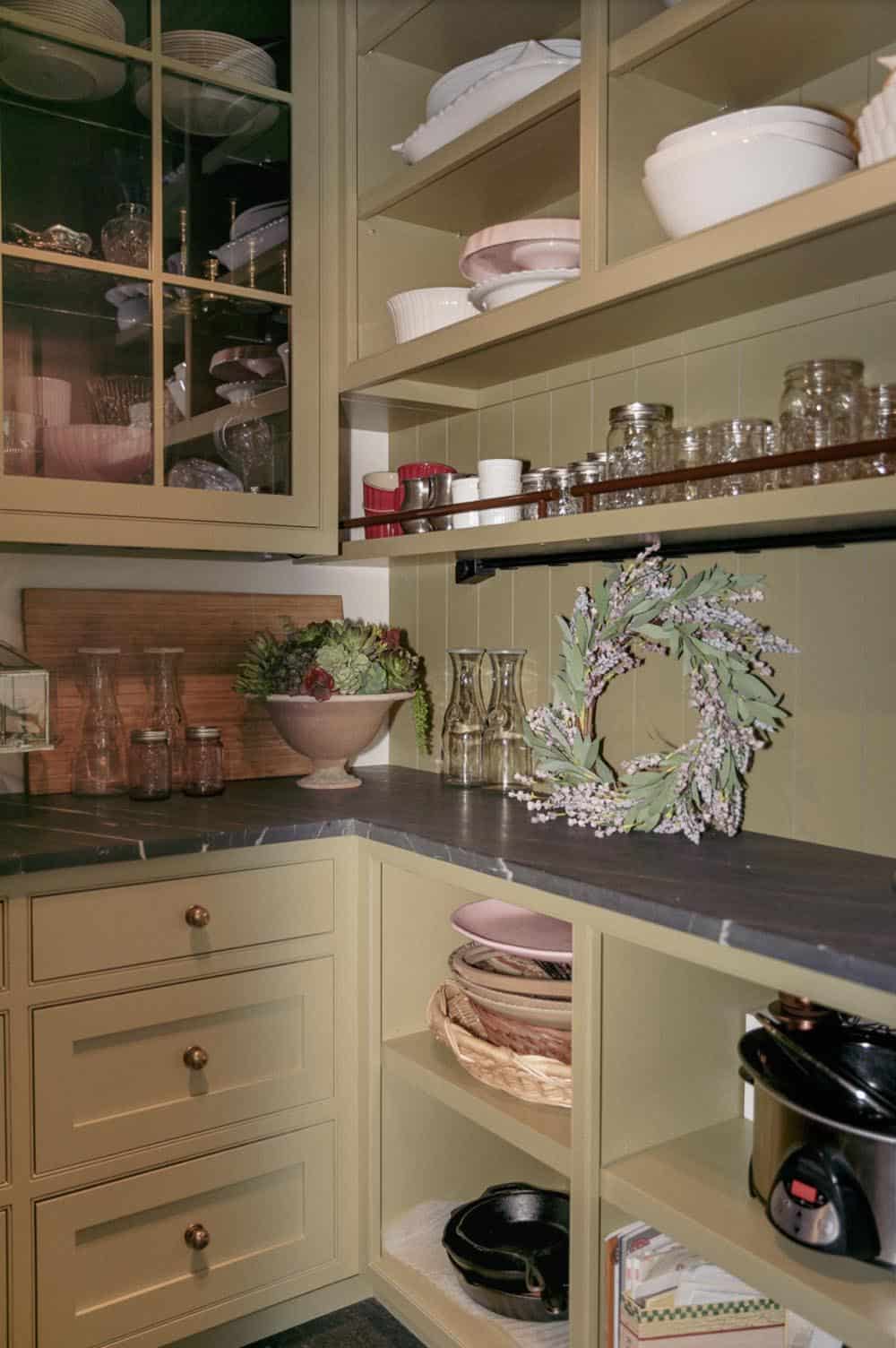 Sage green butler's pantry shelves with jars, dishware, and a floral wreath