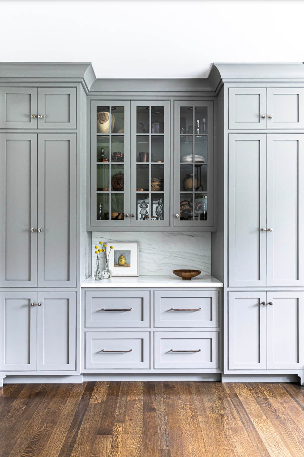 Gray built-in hutch with glass-front upper cabinets and marble backsplash