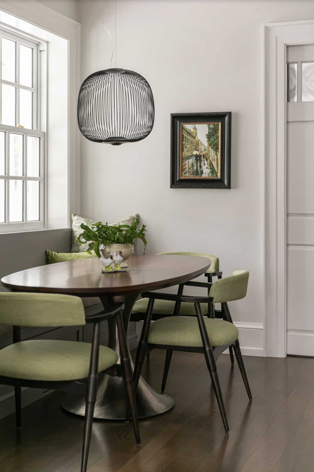 Breakfast nook with a round wood table, olive green chairs, and black wire pendant light