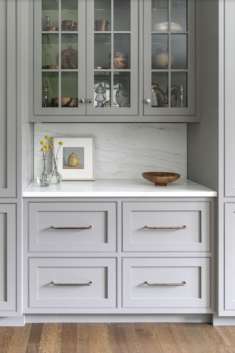 Gray glass-front cabinet detail with silver collectibles and marble backsplash