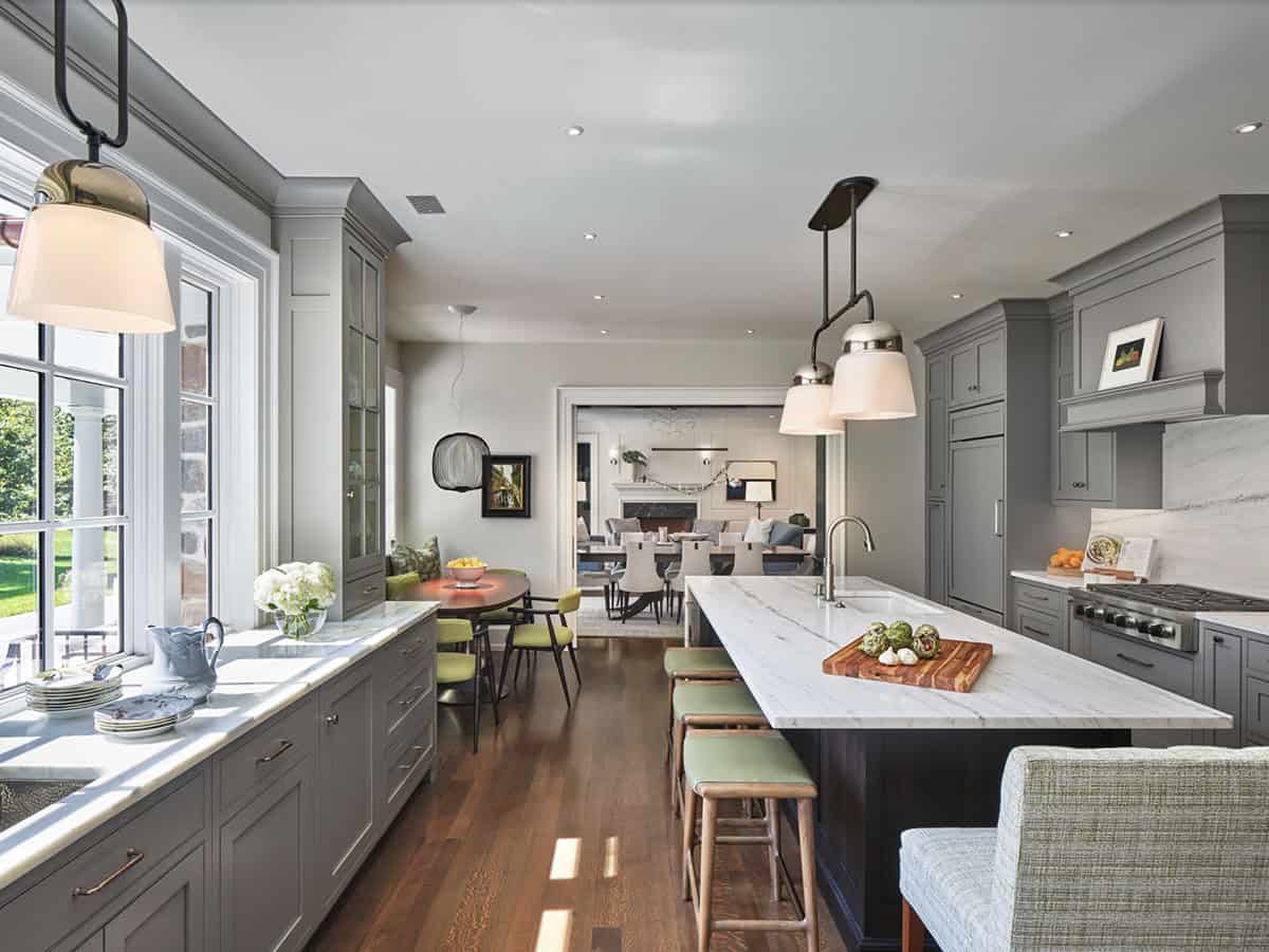 Long kitchen with gray cabinetry, marble island, and view to dining and living areas