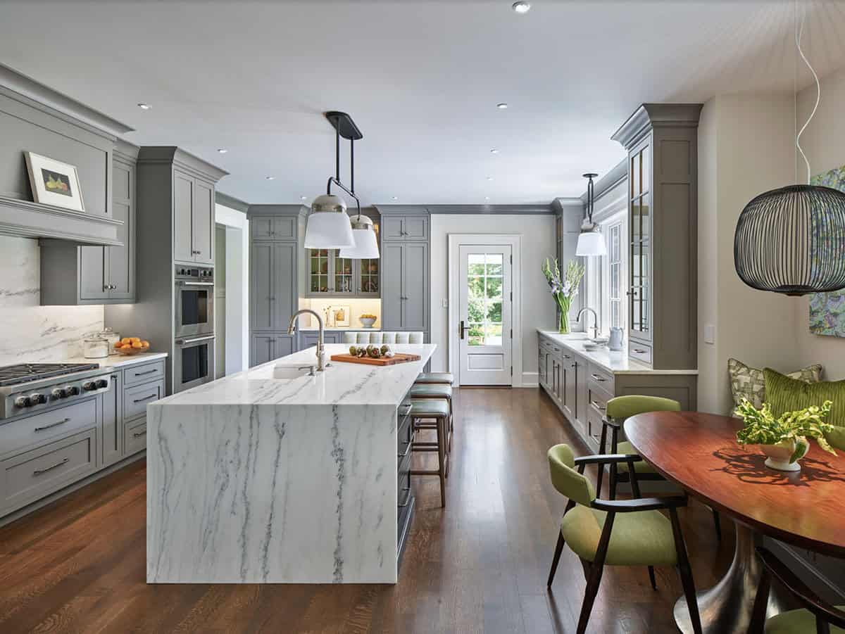 Kitchen island with waterfall marble countertop, gas range, and breakfast nook beyond