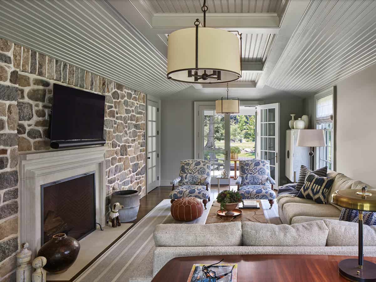 Living room with fieldstone fireplace wall, beamed ceiling, and blue floral armchairs