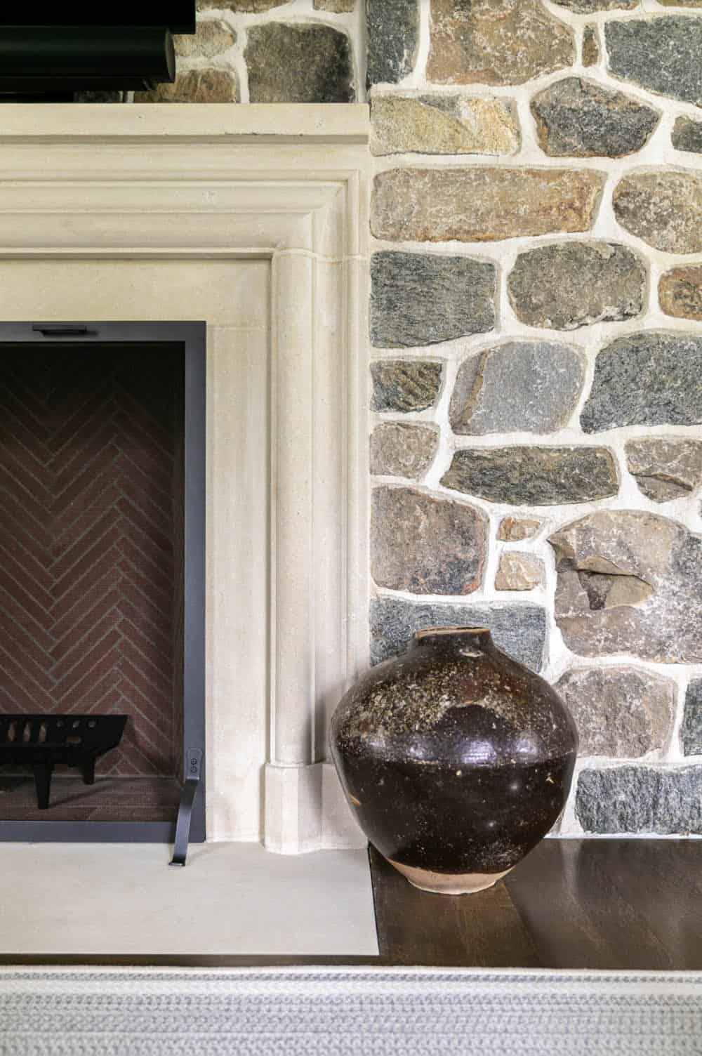 Close-up of stone fireplace surround with carved mantel and dark ceramic vessel