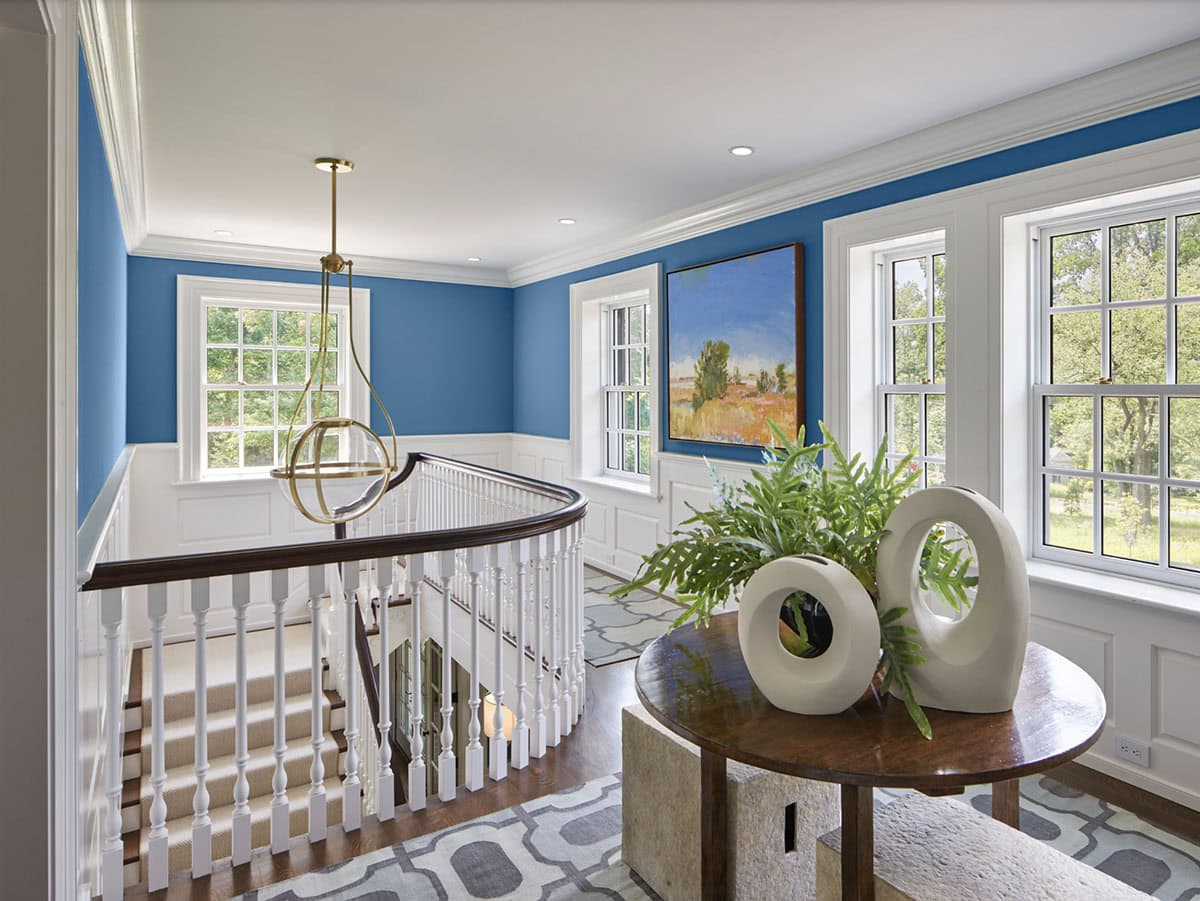 Upper landing with blue walls, curved white railing, and round console table with sculptural vases