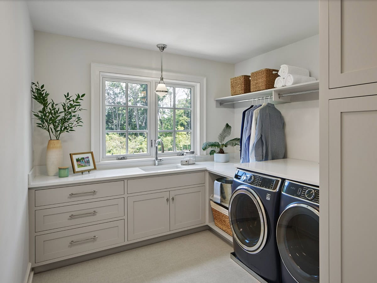 Laundry room with taupe cabinetry, farmhouse sink, and navy front-load washer and dryer