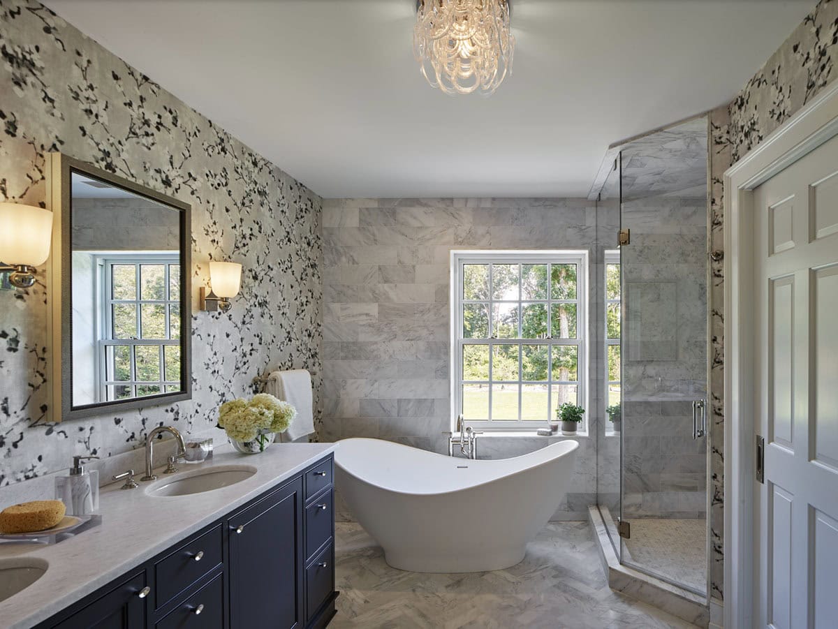 Primary bathroom with floral wallpaper, navy vanity, freestanding tub, and glass shower