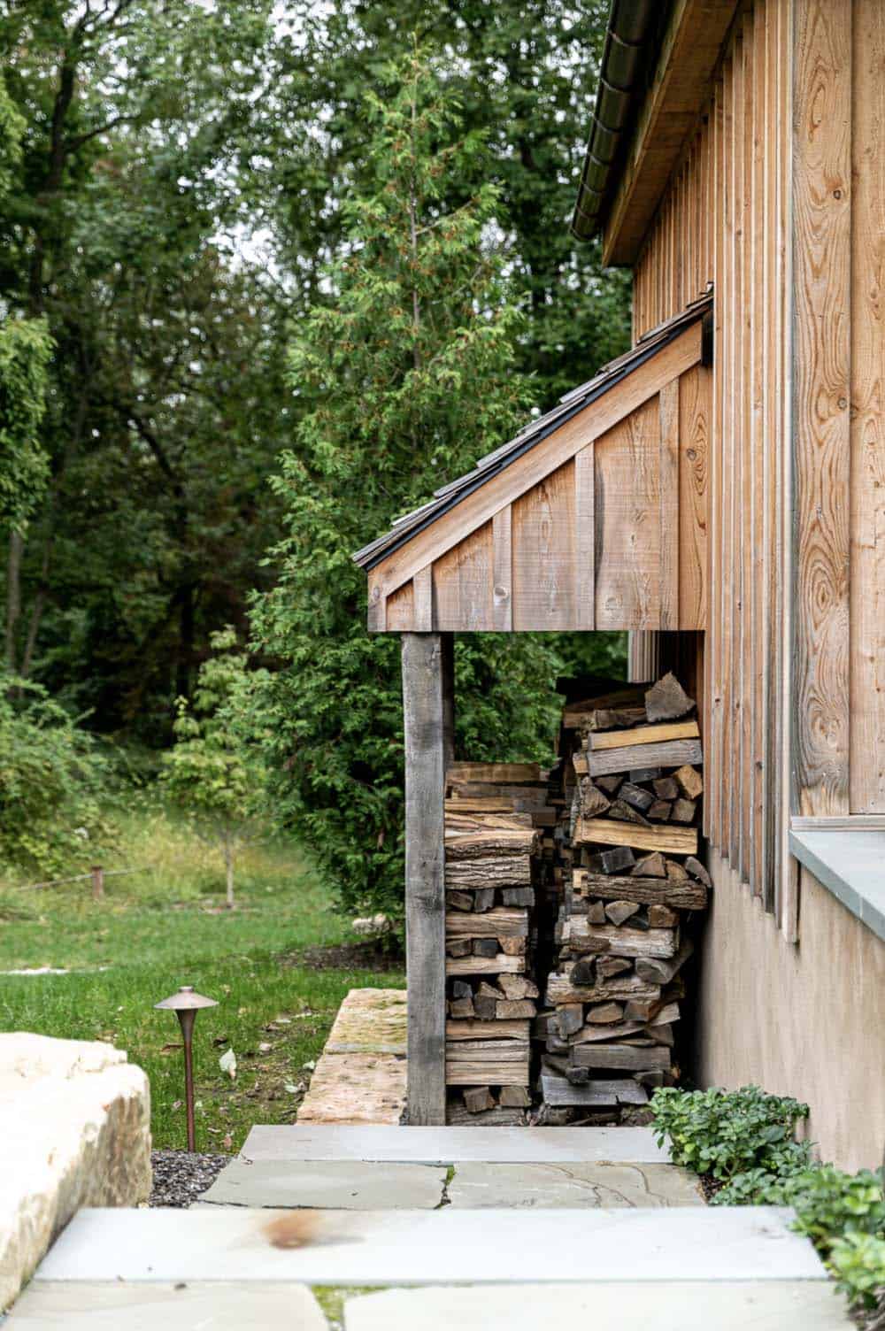 Firewood stacked under a lean-to shelter beside the guest cabin's board-and-batten siding