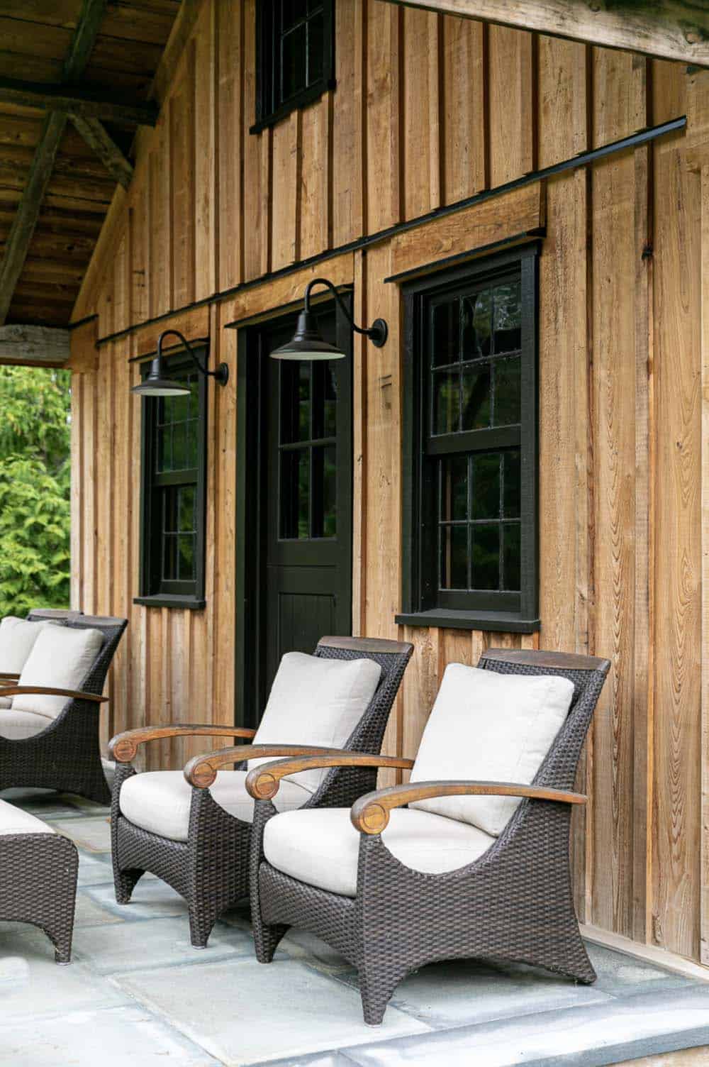 Woven wicker porch chairs beneath black-framed windows and gooseneck sconces on cabin exterior