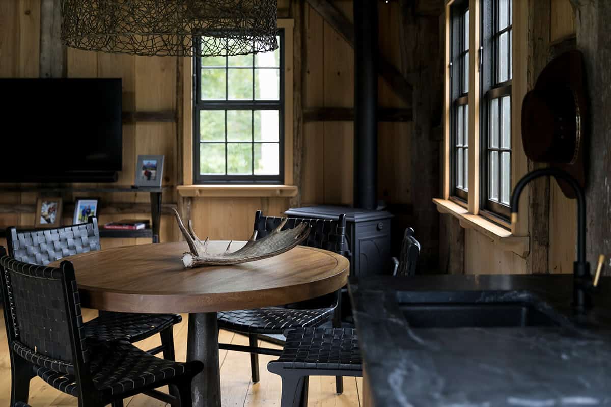 Round dining table with antler centerpiece and woven black leather chairs in timber-frame cabin