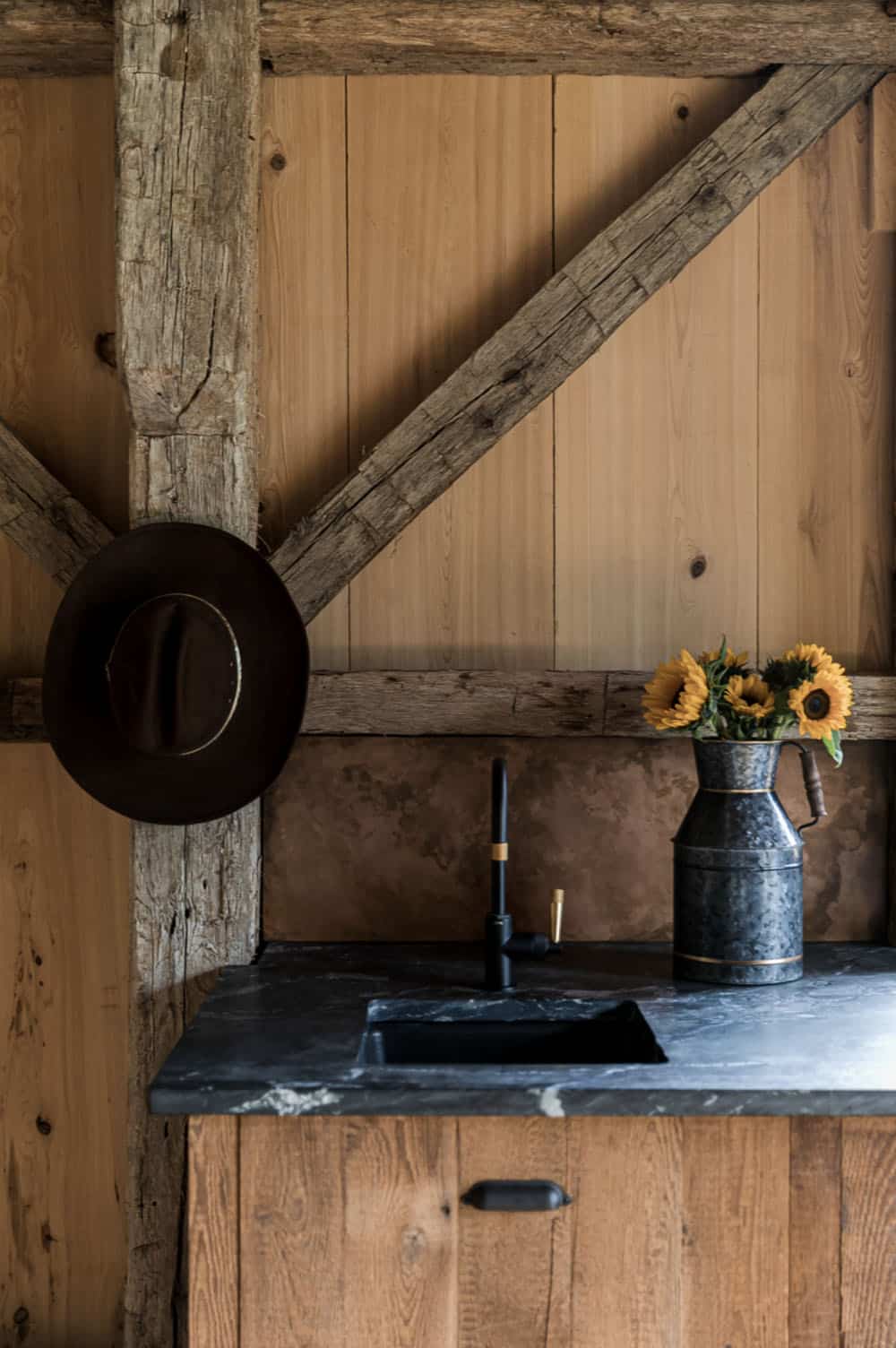 Rustic wet bar nook with soapstone counter, black faucet, and sunflowers in a galvanized pitcher