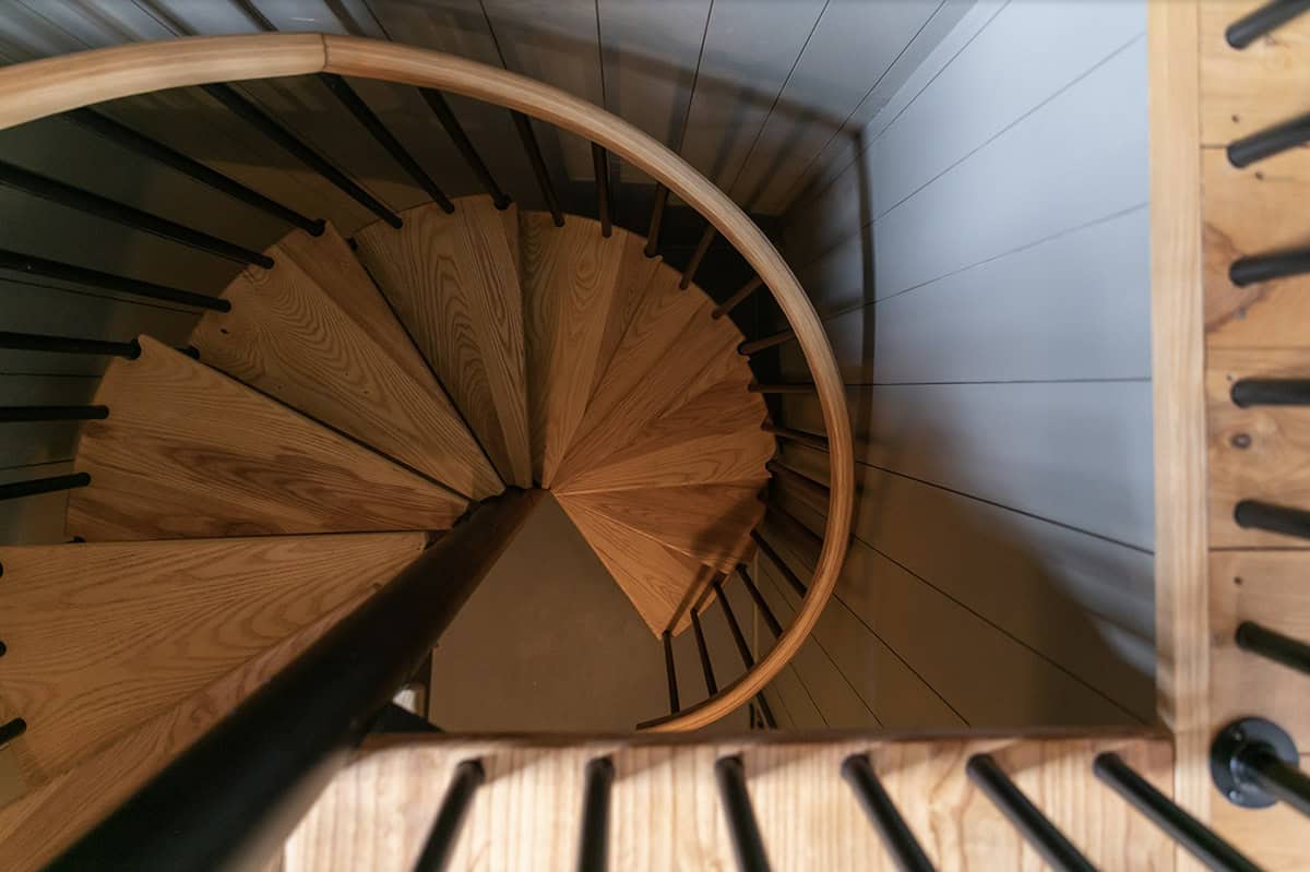Overhead view down a curved wooden spiral staircase with black metal railings