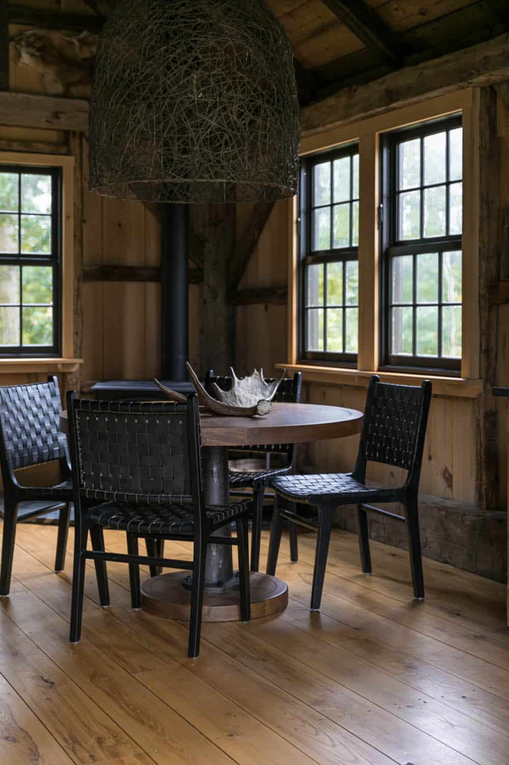 Round wood dining table with antler and woven leather chairs beneath a woven pendant light
