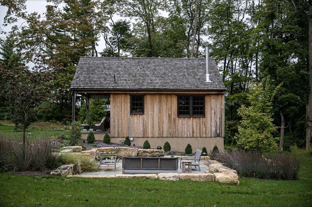 Guest cabin exterior with cedar-shake roof, board-and-batten siding, and stone patio seating area