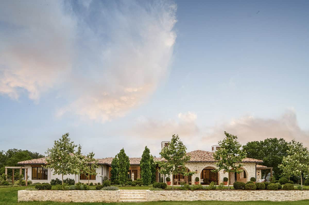 Mediterranean-style stone home with terracotta roof and arched loggia entrance, seen from the front lawn