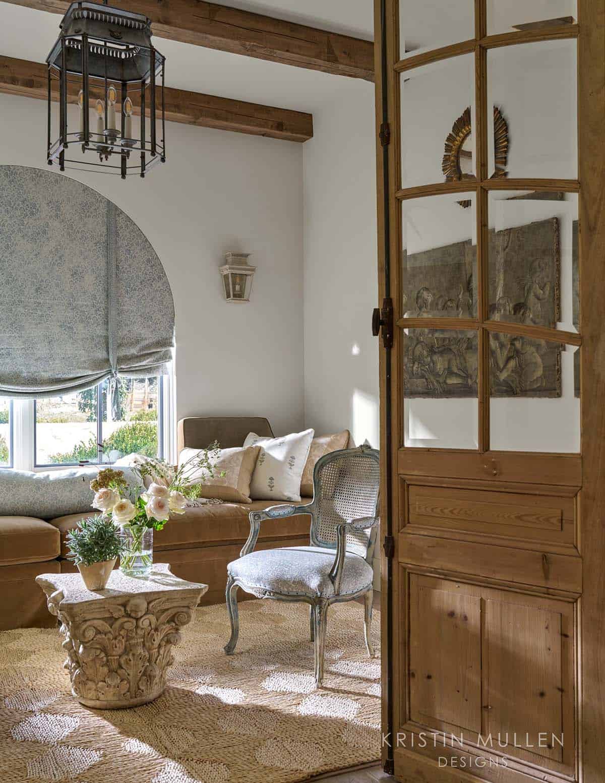Cozy window seat nook with blue and tan patterned pillows, cane-back chair, and antique wall relief through open pine doors