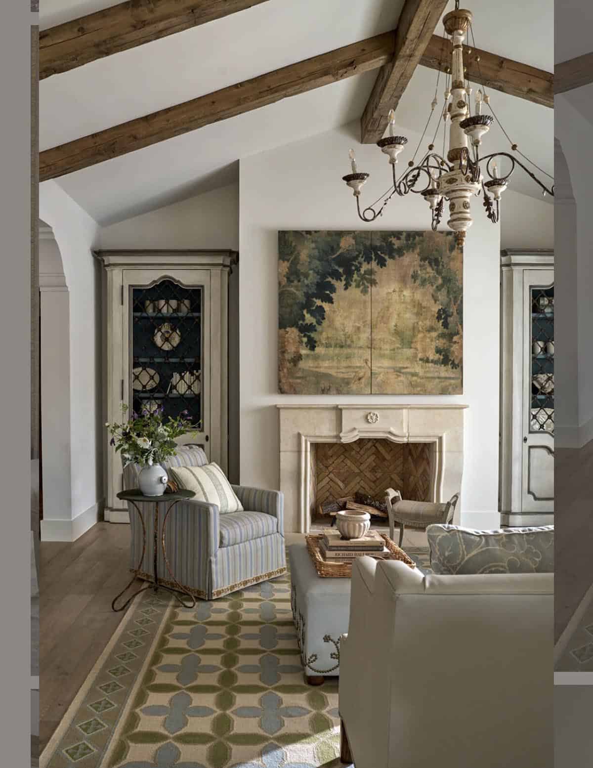 Living room fireplace with stone mantel, framed botanical artwork, wrought-iron chandelier, and antique cabinet