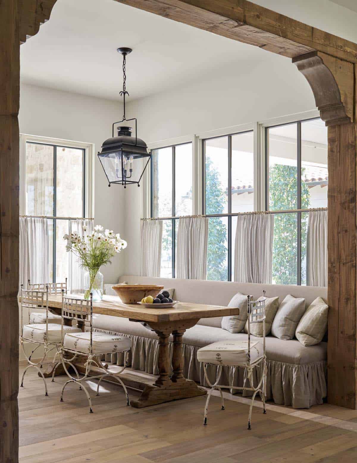 Breakfast nook with rustic wood beams, wood trestle table, iron chairs, upholstered banquette, and lantern pendant light