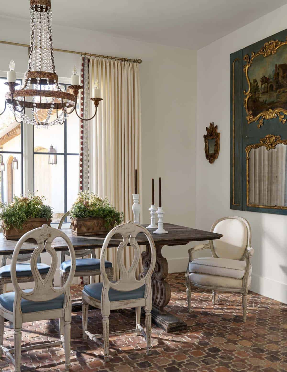 Dining room corner with beaded chandelier, gilt-framed art panel, small mirror, and blue-cushioned French chairs