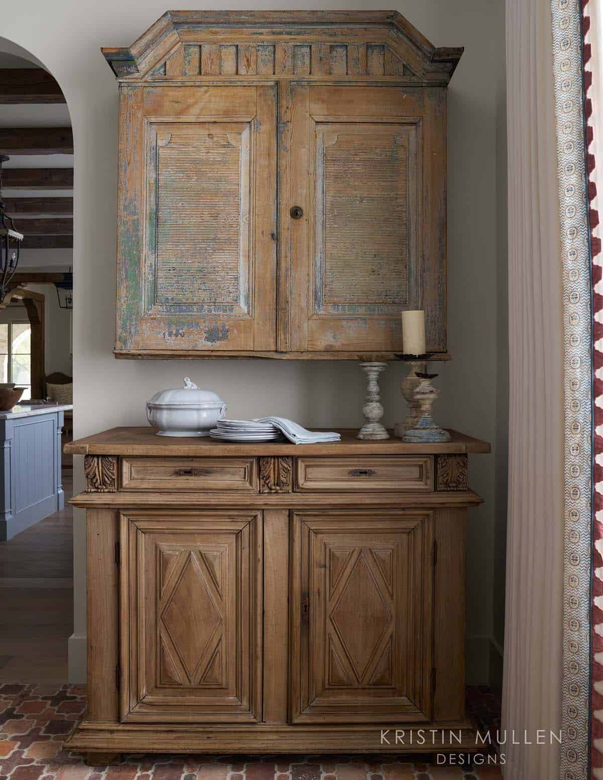 Antique weathered wood cabinet with distressed paint mounted above a carved wooden sideboard with candlesticks and dishware