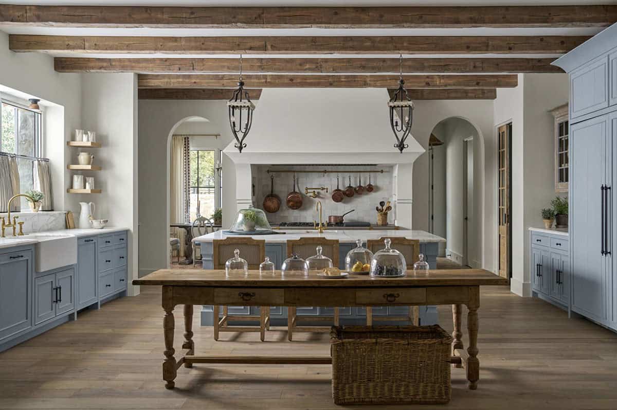 Kitchen island with hanging lanterns, copper pots over the range, and a wood table with glass cloches in the foreground