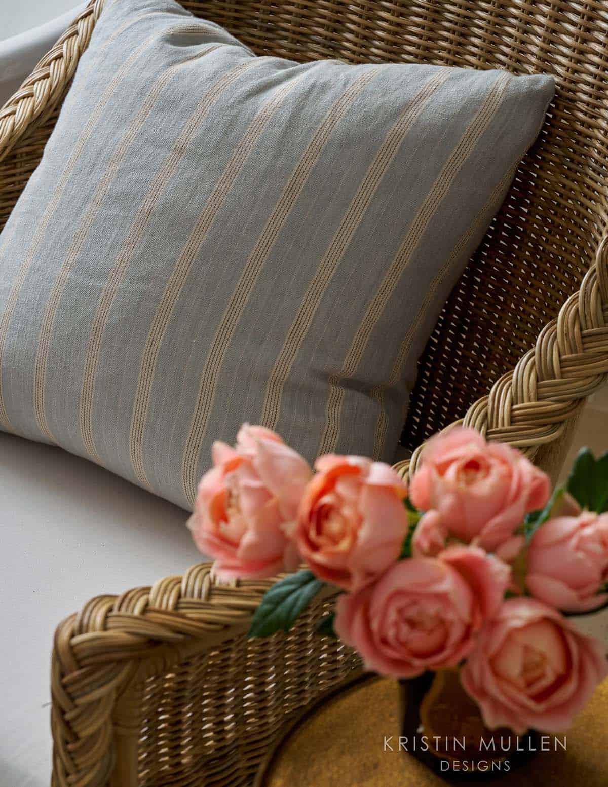 Close-up of a striped throw pillow and pink roses on a woven wicker chair