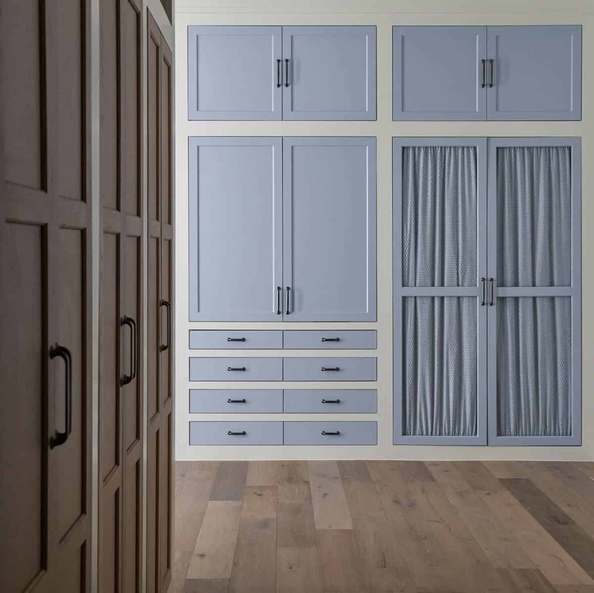Built-in closet with powder-blue cabinetry, paneled doors, sheer curtained cabinet fronts, and wood-tone wardrobe alongside