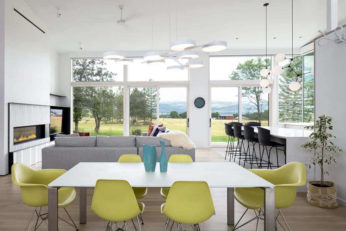 Open-plan living and dining room with yellow chairs, gray sectional, and floor-to-ceiling windows facing mountain views
