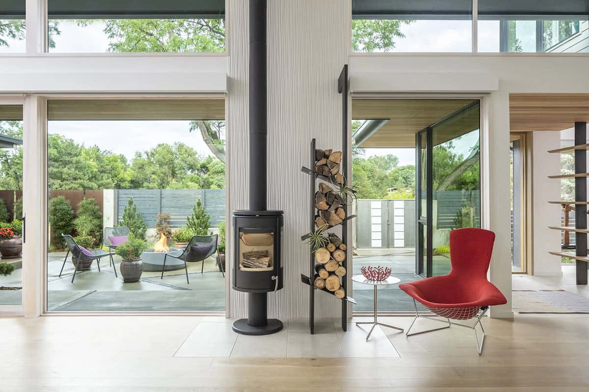 Living room with wood-burning stove, log storage rack, and red modern accent chair beside glass doors to patio