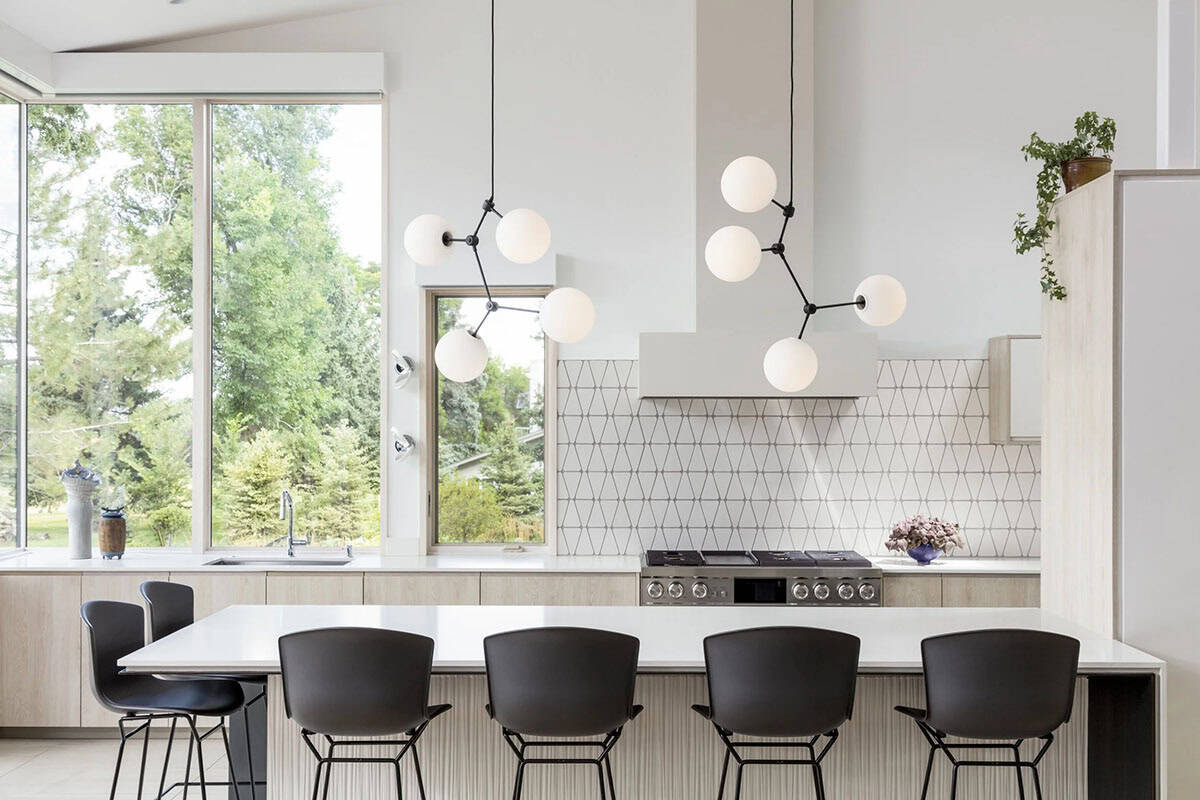 Kitchen island with black barstools, sphere pendant lights, and geometric tile backsplash behind a gas range