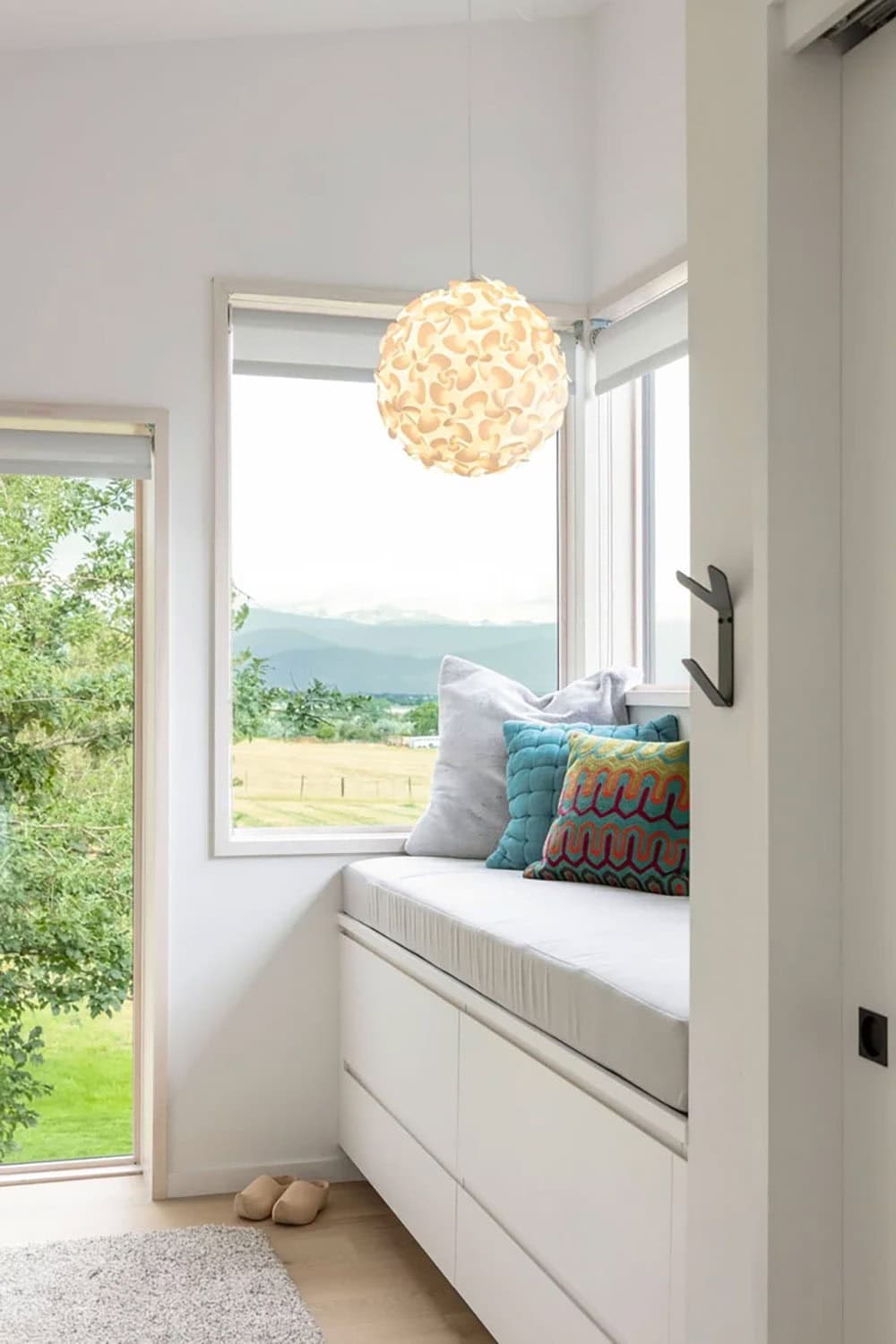 Cozy window reading nook with built-in storage bench, colorful throw pillows, and a spherical pendant light