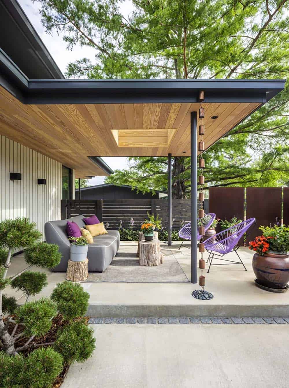 Covered patio seating area with gray sofa, purple accent chairs, and copper rain chain under a wood ceiling