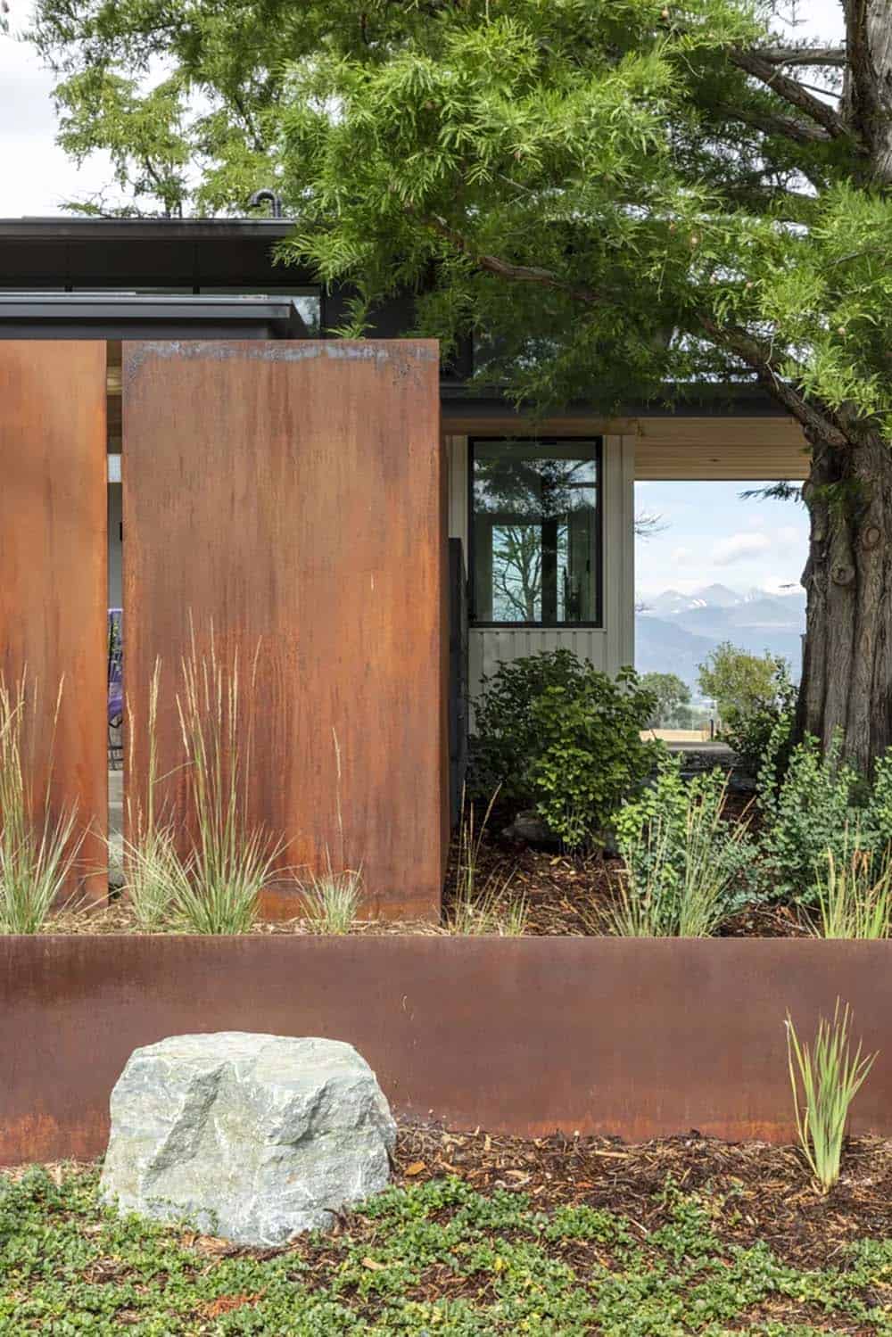 Corten steel garden wall and privacy panels with ornamental grasses and a large boulder accent