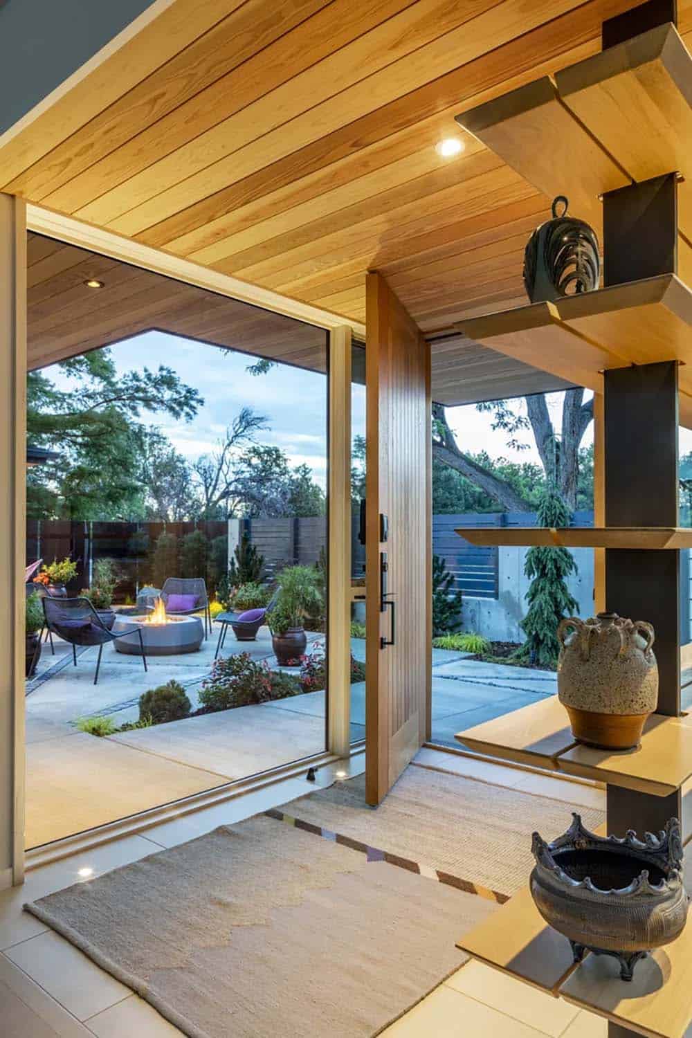 Entryway with wood-slat ceiling, open front door, and tiered wooden shelving displaying ceramic decor