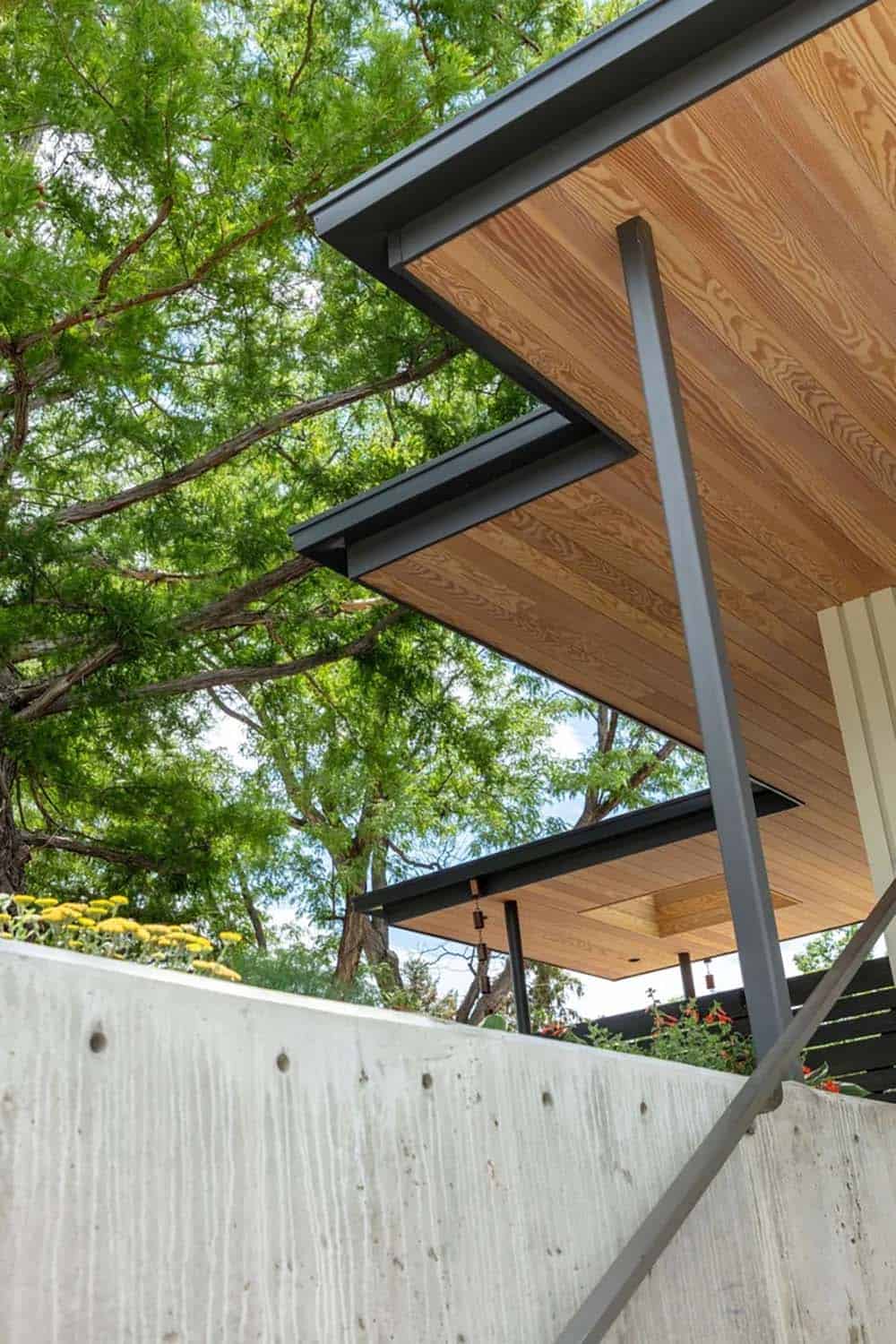 Upward view of angular cedar-lined roof eaves against a backdrop of green trees