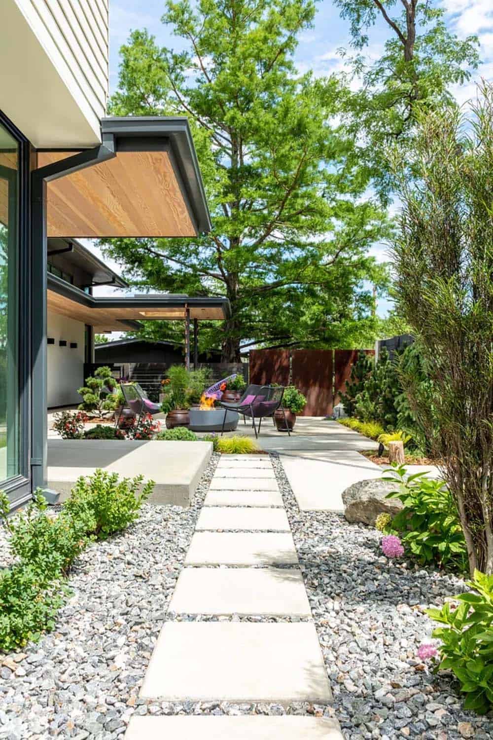 Backyard pathway of concrete pavers set in gravel, leading past a fire pit lounge to a corten steel screen