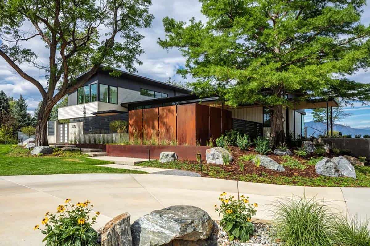 Front exterior of a modern home with corten steel entry screen, black-framed windows, and boulder landscaping