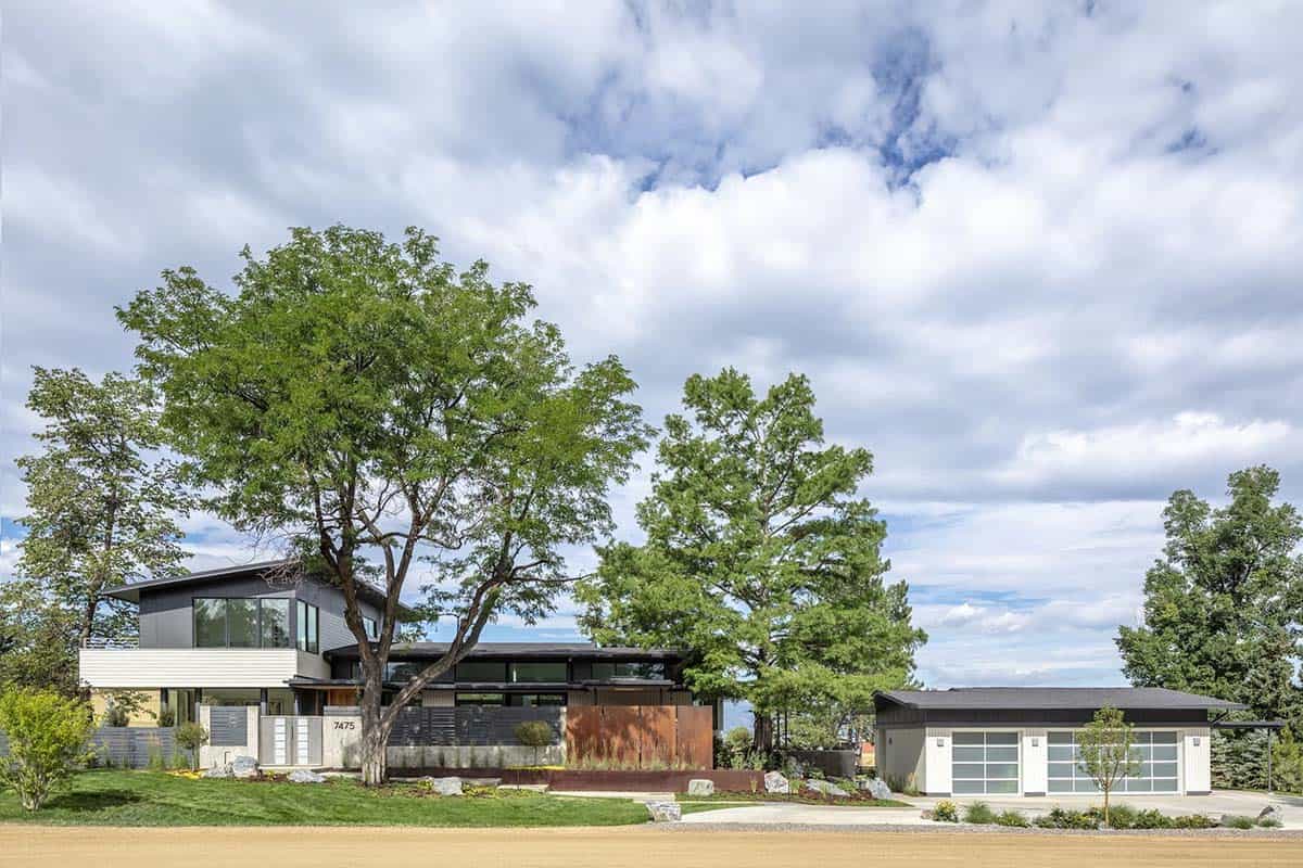 Wide view of a modern home and detached garage nestled among mature trees under a cloudy sky