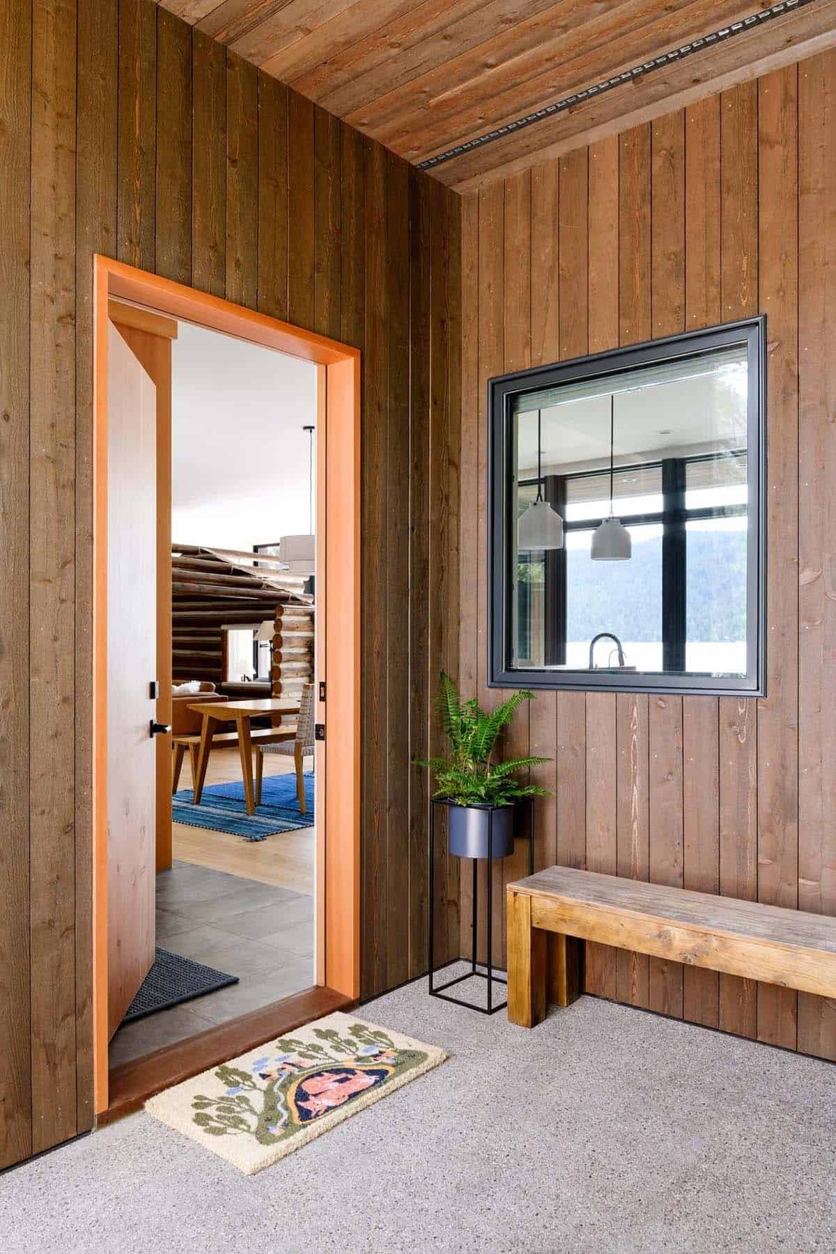 Wood-paneled entryway with orange door frame, potted fern, wood bench, and window overlooking the lake